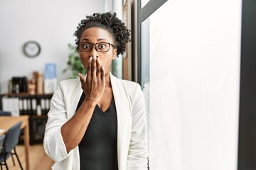 African business woman working at the office covering mouth with hand, shocked and afraid for...