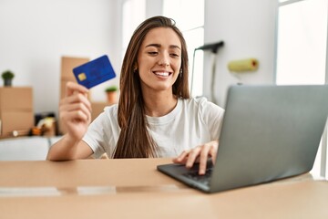 Young hispanic woman smiling confident using credit card and laptop at new home