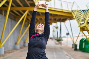 Young hispanic woman wearing sportswear stretching arms at street