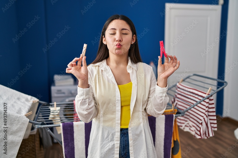 Poster Young latin woman holding clothespins hanging clothes on clothesline looking at the camera blowing a kiss being lovely and sexy. love expression.