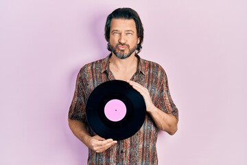 Middle age caucasian man holding vinyl disc looking at the camera blowing a kiss being lovely and sexy. love expression.