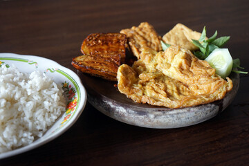 Eggs, tempeh and eggplant penyet with white rice on a wooden table, Indonesian cuisine