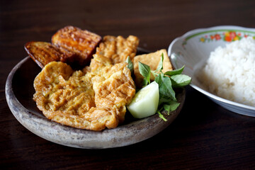 Eggs, tempeh and eggplant penyet with white rice on a wooden table, Indonesian cuisine