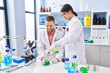 Man and woman wearing scientists uniform pouring liquid on test tube at laboratory