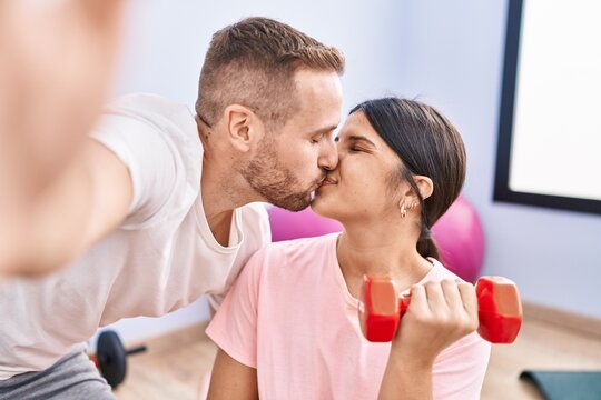 Man and woman couple training using dumbbells make selfie by the camera at sport center