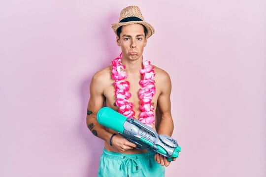 Young hispanic man wearing swimsuit and watergun depressed and worry for distress, crying angry and afraid. sad expression.