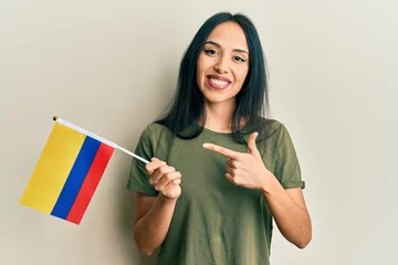 Fototapeten Young hispanic girl holding colombia flag smiling happy pointing with hand and finger © Krakenimages.com