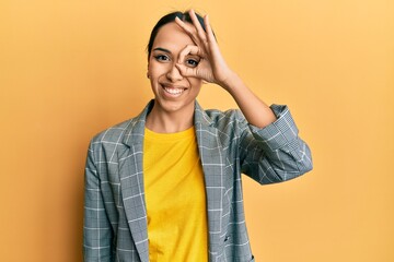 Young hispanic girl wearing business clothes smiling happy doing ok sign with hand on eye looking through fingers