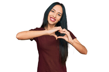Young hispanic girl wearing casual t shirt smiling in love doing heart symbol shape with hands. romantic concept.