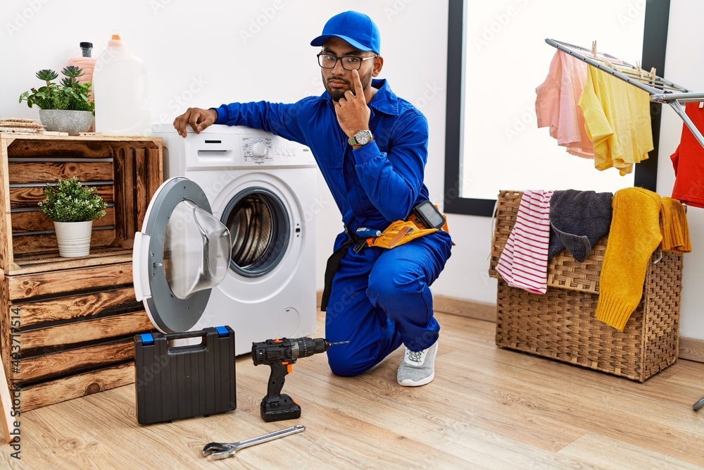 Poster Young indian technician working on washing machine pointing to the eye watching you gesture, suspicious expression