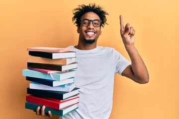 Young african american man with beard holding a pile of books smiling with an idea or question...