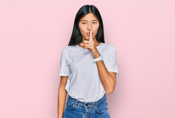 Beautiful young asian woman wearing casual white t shirt asking to be quiet with finger on lips. silence and secret concept.