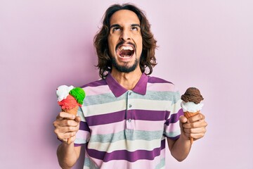 Young hispanic man holding ice cream angry and mad screaming frustrated and furious, shouting with anger looking up.