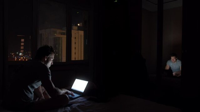 Man working on a laptop in a dark hotel room 1