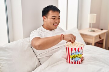Fototapeta na wymiar Young chinese man watching movie sitting on bed at bedroom