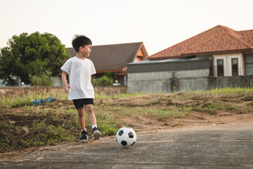 A 6 years old Asian boy kicking the ball as playing outdoor.