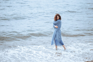 a curly-haired girl in a blue dress dreamily walks on the sea