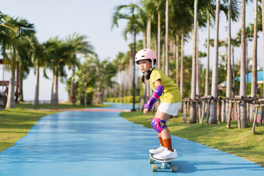 asian child or kid girl playing surf skate or skateboard in skating rink track and extreme sports to wearing helmet elbow pads wrist and knee support for body safety protect at bang phra public park