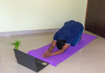 Top view at fit sporty healthy Indian man sitting on a mat in a Yoga pose, doing breathing...