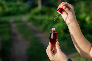 selective focus red facial serum bottle in Asian woman's hand nature background There is space for text.