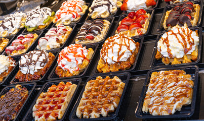 Delicious traditional Liege waffles with colorful toppings on display in a store window in Brussels, Belgium. Sugary desserts. Typical Belgian sweet food.