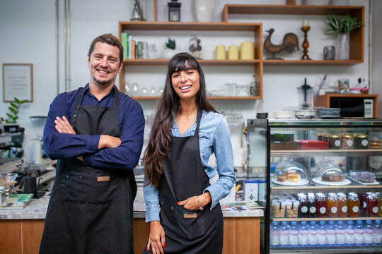 Portrait of smiling owner man standing at his cafe. Coffee owner standing with apron in coffee shop to welcome customer.