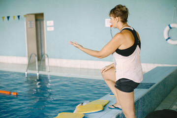 Mature woman coach with whistle by poolside