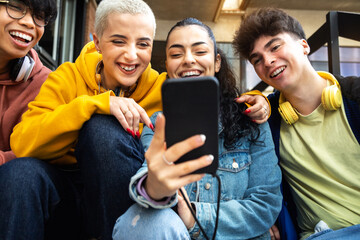 Happy college student friends look mobile phone laughing together. Multiracial teenagers using...