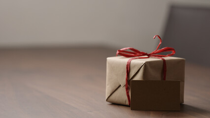 brown paper gift box with red bow on wood table with blank paper card