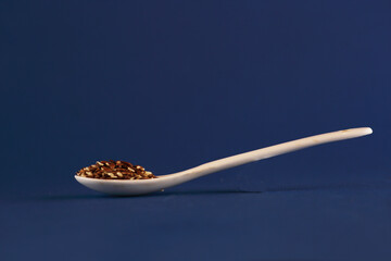 porcelain spoon of beniseed and linseed isolated on blue background