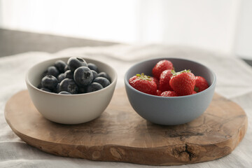 Two bowls with fresh blueberries and strawberries on woo dboard
