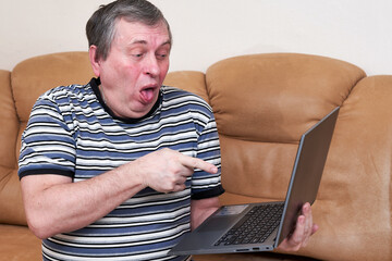 A freak with a surprised face holds a laptop in his hands while sitting on couch - 493730776