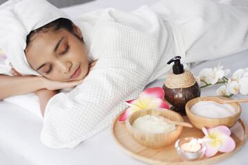 Obraz na płótnie Canvas Smiling Asian woman in white bathrobe and headscarf and lie down. She close her eyes and relax on bed preparing for massage therapy at alternative medicine healing spa Center in Thailand