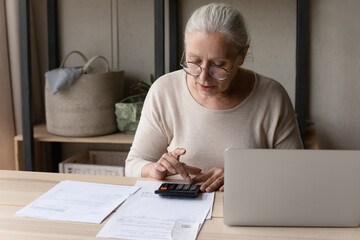 Personal finances management, accounting concept. Older woman in glasses sitting at table using...