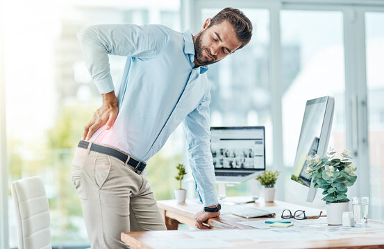 I need to work on my posture to prevent this pain. Shot of a young businessman suffering with back pain while working in an office.