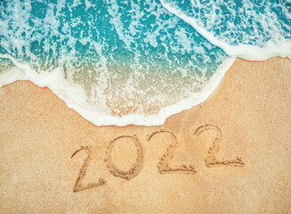 New Year 2022 written on seashore sand at sunrise concept.beautiful sandy beach and soft blue ocean wave
