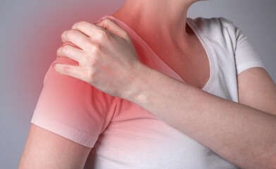 Woman suffering from shoulder pain. Hand holding shoulder with red spot closeup. Health problems, medicine concept. High quality photo