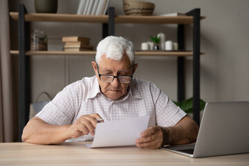 Serious focused elderly man wear glasses holding paper, read received formal document, learning...