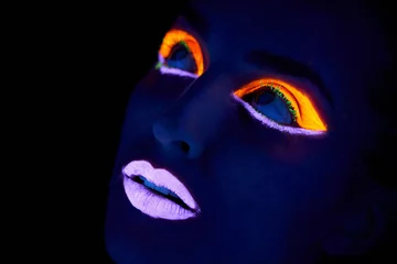 Bright eyes. A young woman with with neon paint on her face posing. © Tylan E/peopleimages.com
