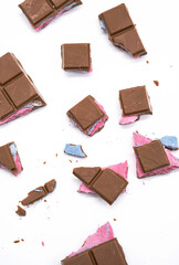 Broken pieces chocolate bar with pink blue filling on white. Crumbled chocolate bar of various size pieces, close up.