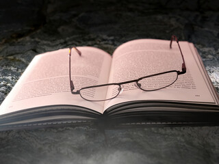 Opened book on a stone slab with an old used reading glasses between the pages with German text