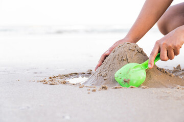 play with sand on summer beach. building sandcastle with plastic shovel, wet sand by water,...