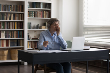 Middle-aged businesswoman sit at desk feels eyestrain takes off glasses rub fatigued eyes. Long...