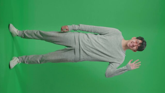 Full Body Of Asian Man Waving Hand And Smiling While Standing On Green Screen In The Studio
