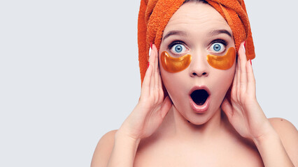 Surprised young caucasian woman with patches under her eyes and a towel on her head holds card product 