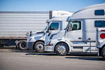 Naklejka premium Profiles of different white big rigs semi trucks with semi trailers standing on the truck stop parking lot taking a break according to the schedule of cargo movement
