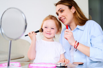 Young happy mom playing with her preschool daughter and doing makeup