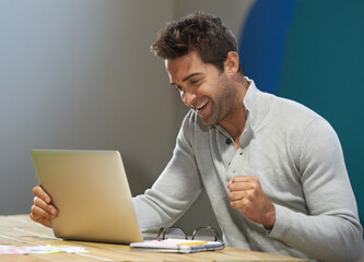 Celebrating a successful startup. A smiling entrepreneur using his laptop at a table.