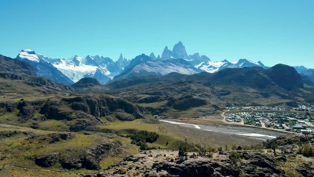 Top cinematic aerial view - Mount Fitz Roy in El Chalten, Patagonia, Argentina, wide shot backward. Hikers on the huge boulders with amazing background.