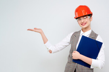 Young female caucasian engineer smiling wearing orange constraction helmet and googles holds blueprint on isolate background